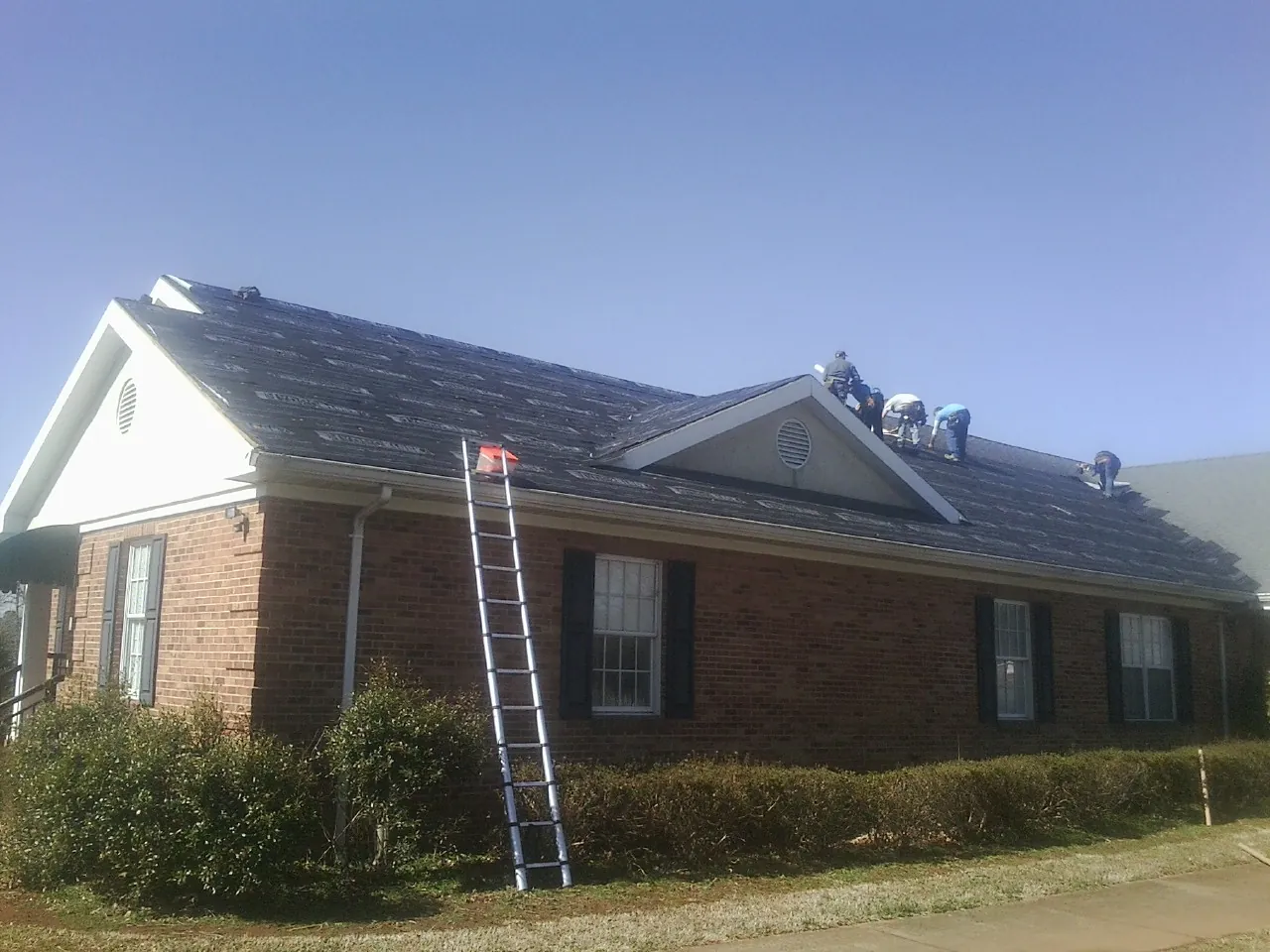 Crew tearing shingles off a brick ranch roof with a ladder set — Metal Roof Repair work by our crew in Tompkinsville