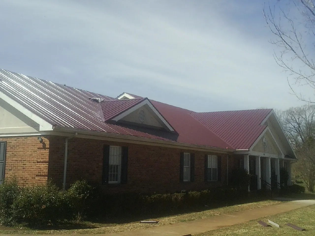 Red metal roof with gabled entries on a long brick building, from a Hail Damage Roof Repair job in Tompkinsville