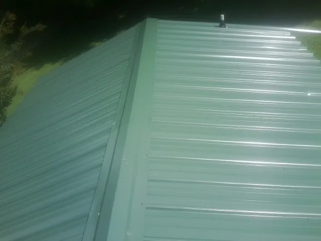 New green metal panels meeting at the ridge of a roof — Flat Roof Repair work by our crew in Tompkinsville