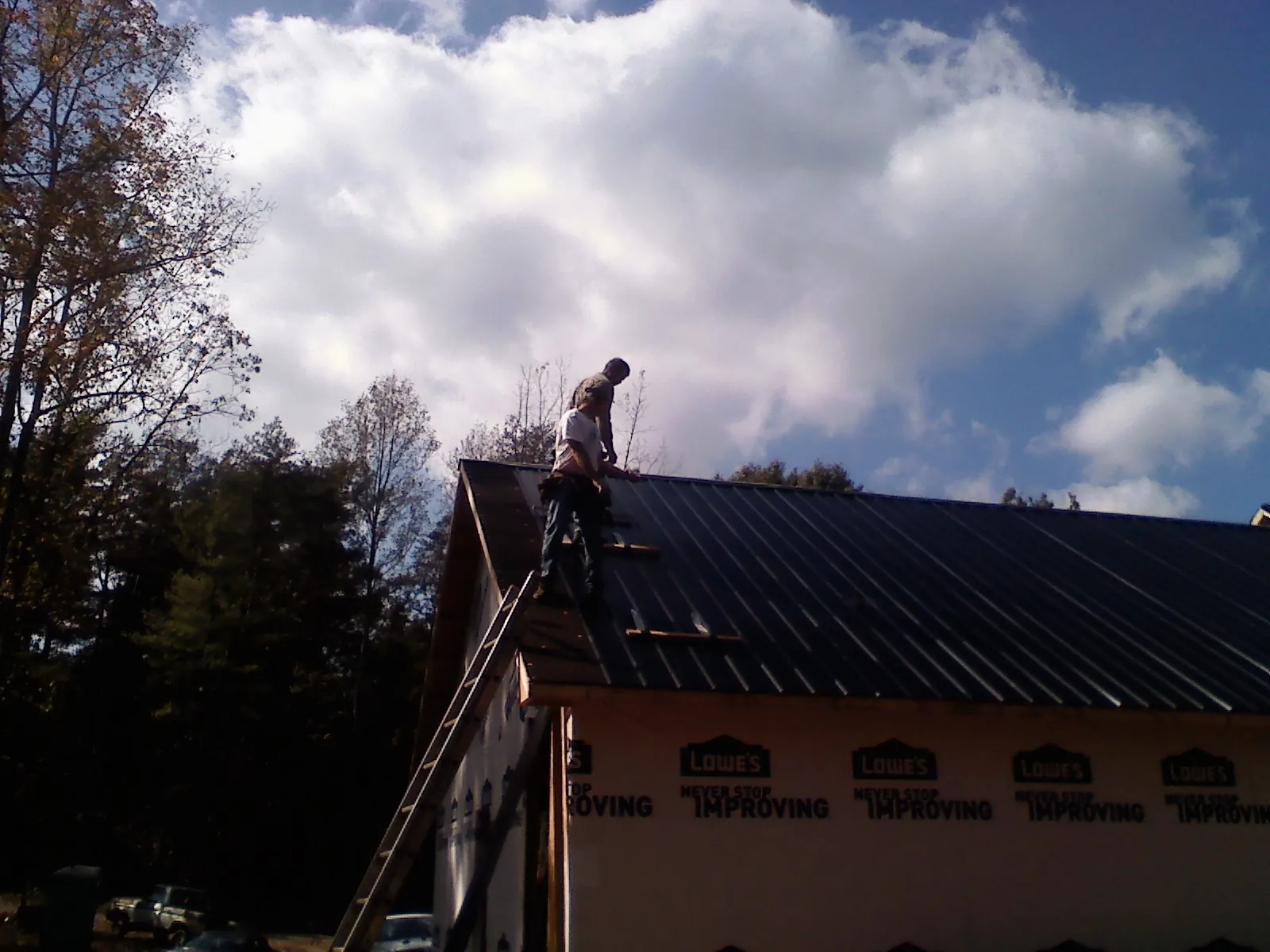 Roofer fastening dark metal panels high against a cloudy sky, from a Roof Inspection job in Tompkinsville