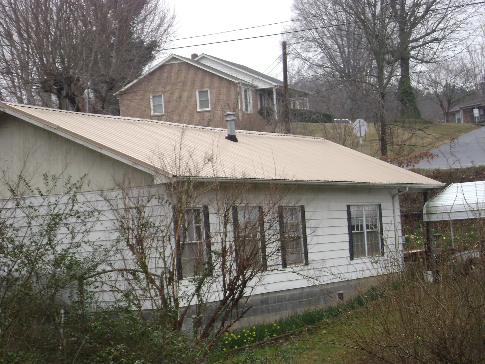 Tan metal roof on a white sided house set into a hillside — Commercial Roofing by Roofing Brothers in Tompkinsville